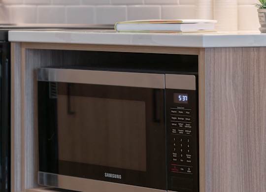 A Samsung microwave oven with digital display and control panel is built into a wooden cabinet.