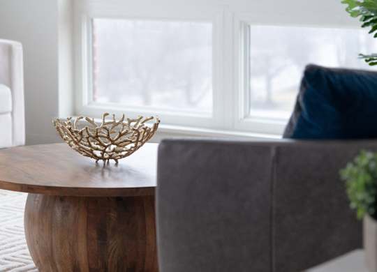 A wooden bowl with a woven handle sits on a wooden table.