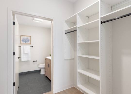 A white bathroom with a toilet and a white closet with shelves.