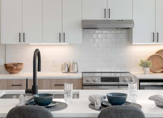 A modern kitchen with a white countertop and a black faucet.