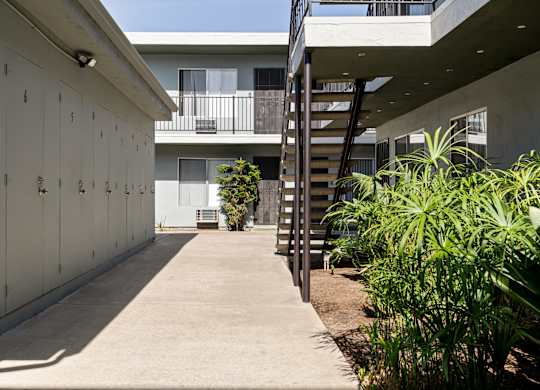 A concrete pathway leads to a building with a balcony and a staircase.
