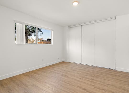 A room with a sliding door and a window with a view of a building and trees outside.