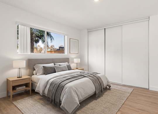 A bedroom with a large bed and a window showing a view of a palm tree.