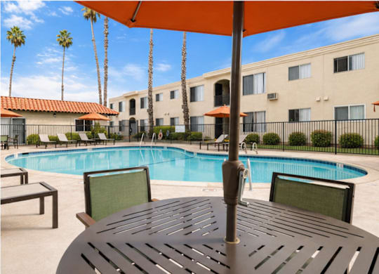A pool with a table and chairs and an umbrella in the foreground.