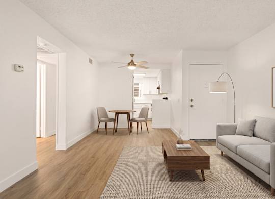 A living room with a grey couch, a wooden coffee table, a dining table with chairs, and a ceiling fan.
