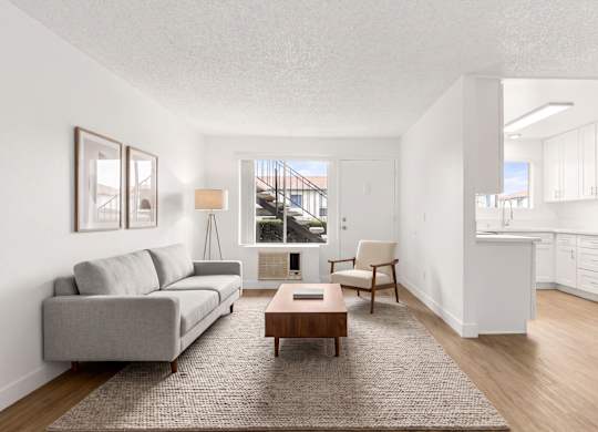 A living room with a grey sofa, a wooden coffee table, and a kitchen area with a refrigerator.