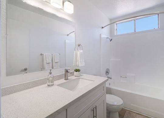 A white bathroom with a sink, mirror, and toilet.