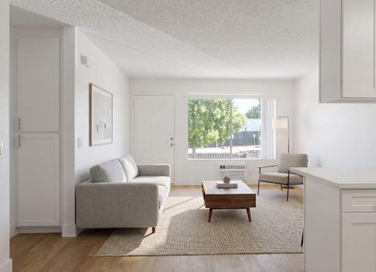 A living room with a grey couch, a coffee table, and a window with a view of trees and buildings outside.
