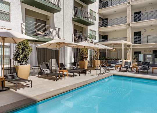 A pool area with chairs and umbrellas in front of a building.