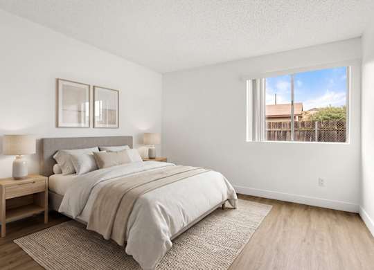 A bedroom with a large bed and a window overlooking a fence.