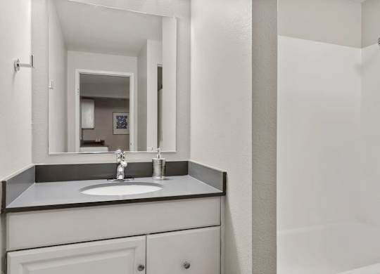 A bathroom with a sink, mirror, and shower.