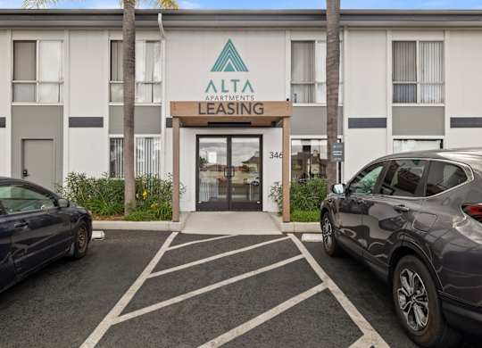 A blue car is parked in front of a building with a sign that reads