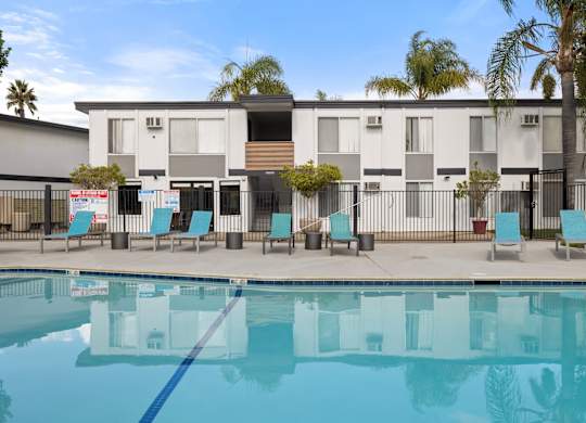 A swimming pool in front of a building with a fence and chairs around it.