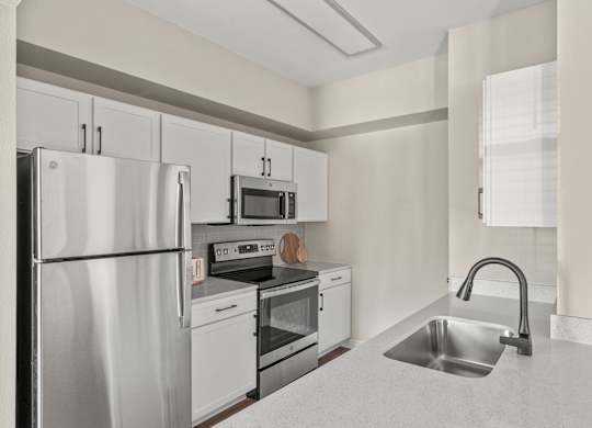 A kitchen with a refrigerator, oven, sink, and microwave.