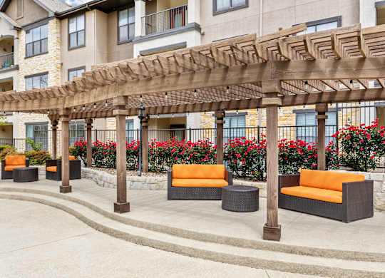 A wooden pergola with orange cushioned seating is in front of a building.