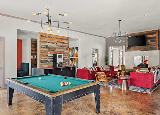 A pool table is in the middle of a room with a red couch and a TV.