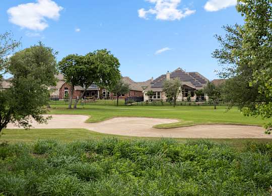 A view of a green field with trees and a building in the background.