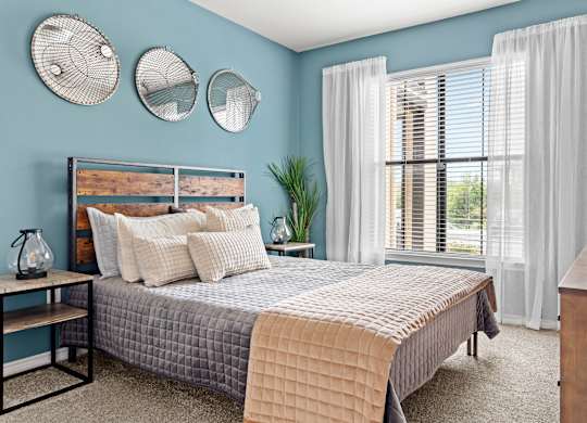 A bedroom with a bed, nightstand, and window with white curtains.