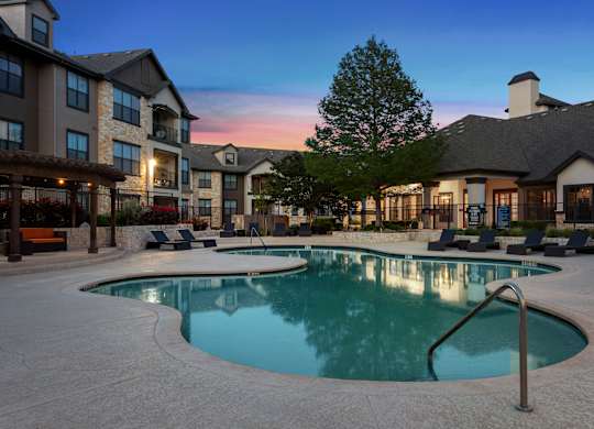 A large outdoor swimming pool surrounded by lounge chairs and buildings.