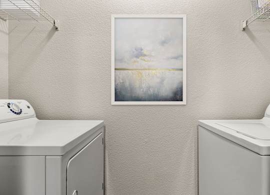 A laundry room with a washing machine and a painting on the wall.