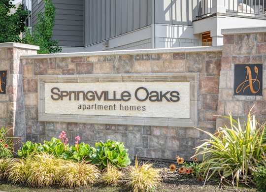 A sign for Springville Oaks apartment homes is displayed in front of a building.