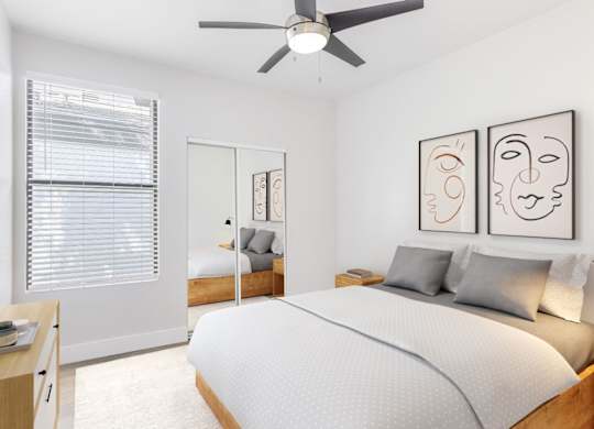 A bedroom with a bed, a nightstand, a window with blinds, a ceiling fan, and two framed artworks on the wall.