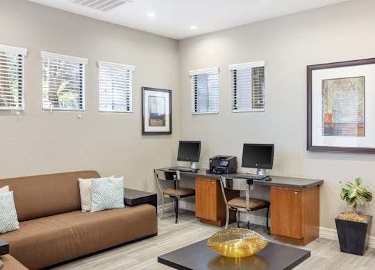 A living room with a brown couch, a desk with a computer, and a framed picture on the wall.