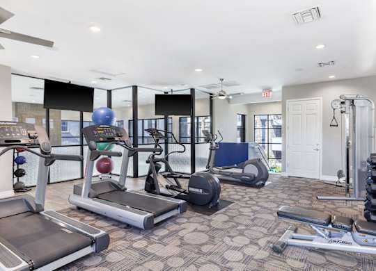 A spacious gym with a variety of equipment including treadmills, elliptical machines, and weight machines.