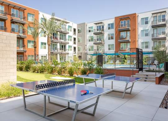 A ping pong table is in the middle of a courtyard with apartment buildings in the background.