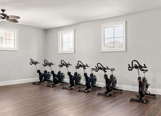 A room with a row of stationary bikes and a ceiling fan.