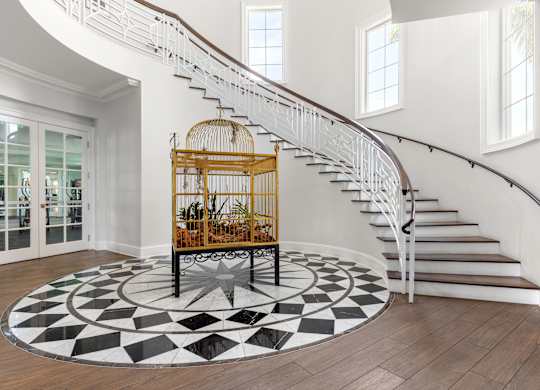 A white staircase with a wooden banister and a birdcage on a circular rug.