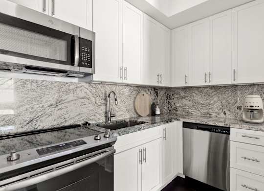 A kitchen with white cabinets and a marble backsplash.