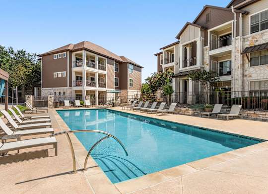 A swimming pool surrounded by lounge chairs in front of apartment buildings.