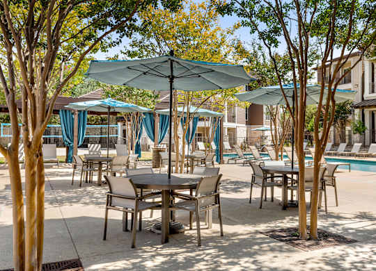 A poolside area with tables and chairs and umbrellas.