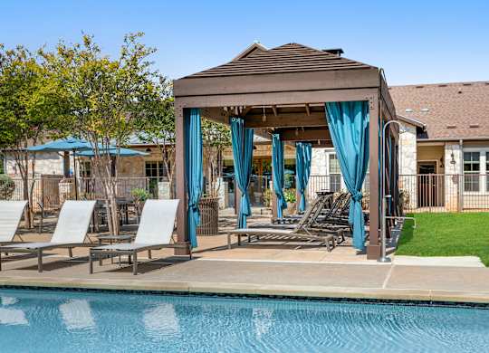 A poolside pavilion with a brown roof and blue curtains.