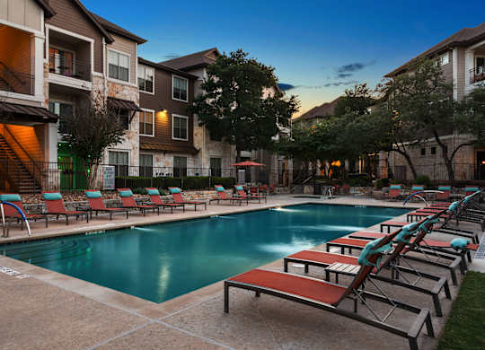 A swimming pool surrounded by lounge chairs and apartment buildings.
