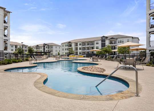 A large outdoor swimming pool surrounded by a concrete patio and chairs.