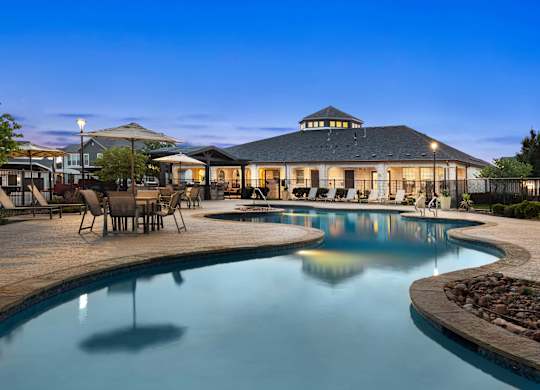 A large swimming pool in front of a building with a patio area.