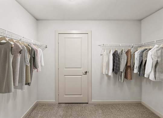 A white door is in a room with clothes hanging on the wall.