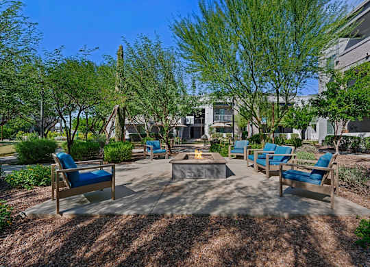 A sunny day at the outdoor seating area of a building with blue chairs and a fire pit.