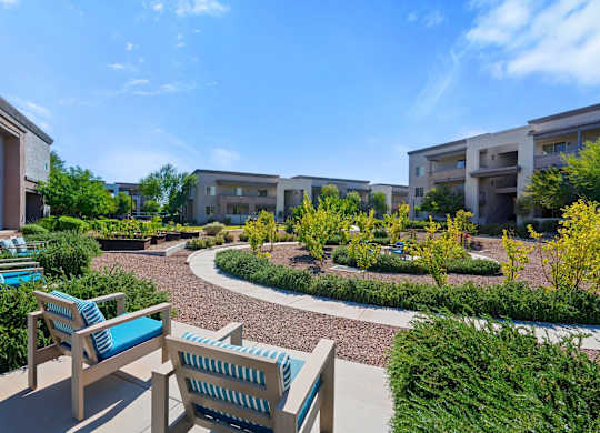 A sunny day at a residential complex with a bench and a chair in the foreground.