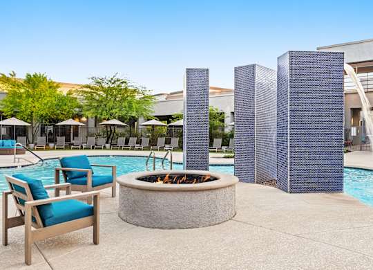 A poolside area with a fire pit, chairs, and umbrellas.