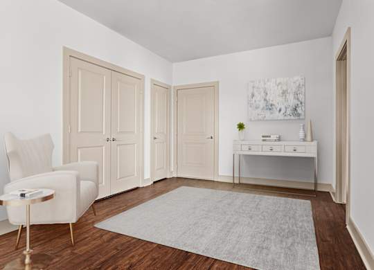 A white chair sits in a room with a grey rug and a painting on the wall.