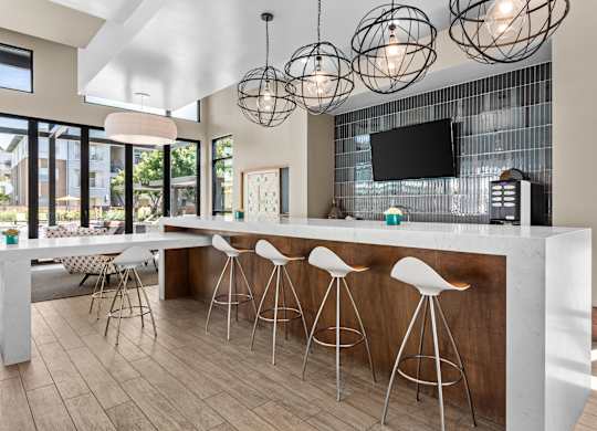 A modern kitchen with a bar area and white stools.