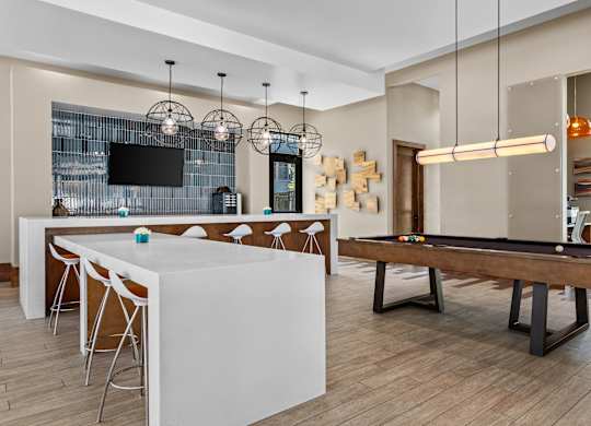 A billiard table is in the middle of a room with a bar and a television.