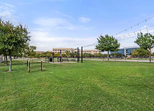 A grassy field with trees and a fence in the foreground and a building in the background.