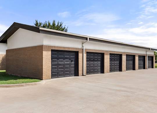 A building with a brown brick facade and a white roof has six black garage doors.
