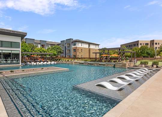 A large swimming pool with lounge chairs is surrounded by buildings.