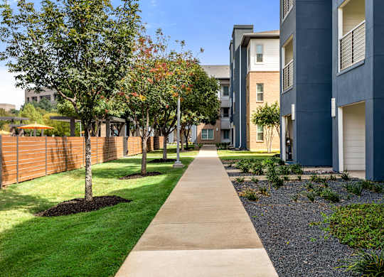 A long concrete walkway separates the grassy area from the apartment buildings.