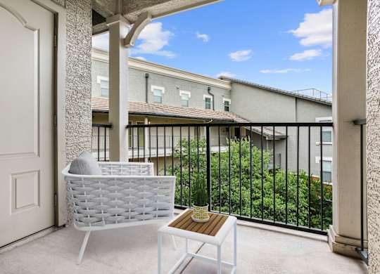 A white chair and table are on a balcony with a view of a building.